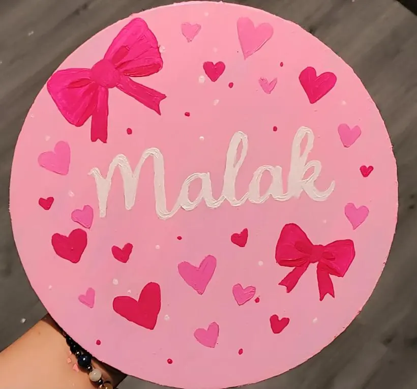 The back of a mirror painted pink with the name Malak, hearts and bows