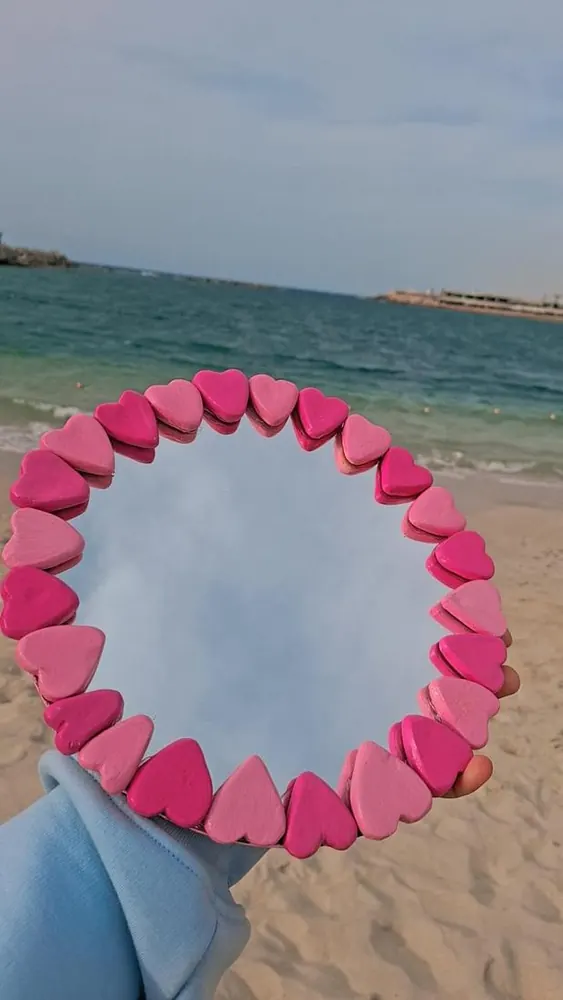 Pink heart mirror held up at the beach